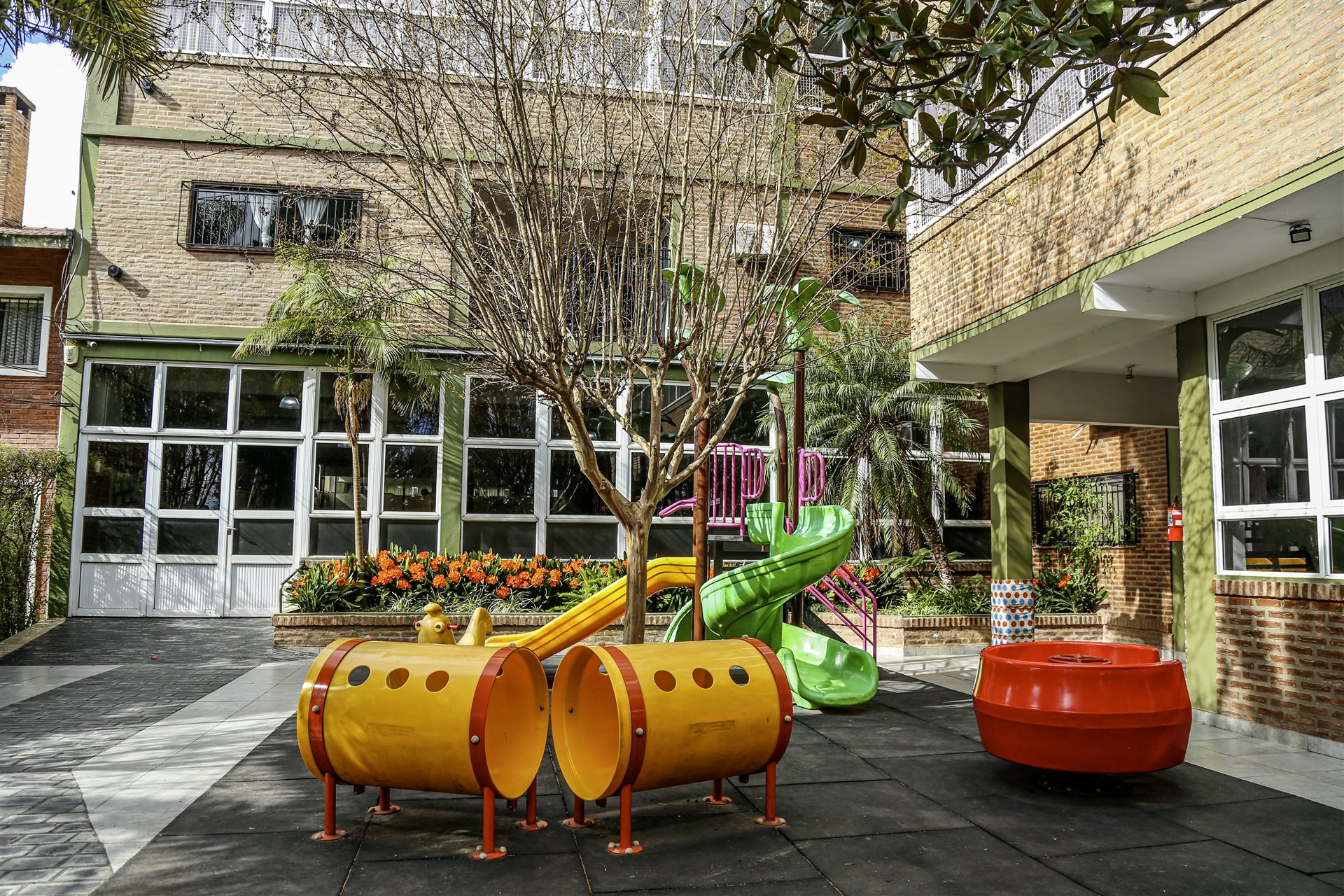 Patio con juegos infantiles de colores, canteros con flores y palmeras